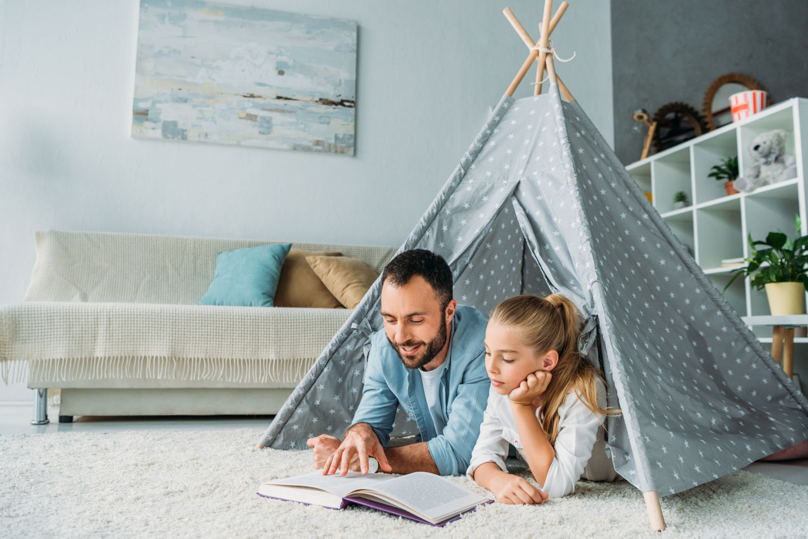 father and daughter lying on floor inside of teepee and reading book together at home